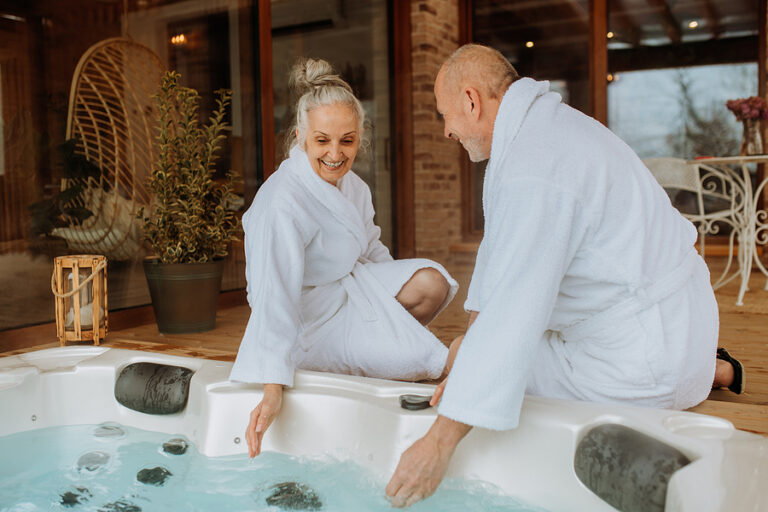 Senior Couple In Bathrobe Checking Temperature In Outdoor Hot Tu